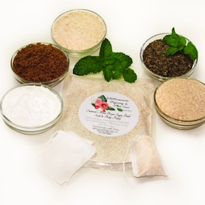 Puede incluir: Una bolsa blanca con una etiqueta que dice "Oatmeal Mint & Brown Sugar Bath Soak & Body Polish" y un gráfico de una flor rosa. La bolsa contiene un polvo blanco y está rodeada de pequeños cuencos que contienen varios ingredientes, incluyendo azúcar moreno, polvo blanco y hojas de té verde.