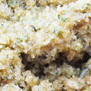 Close-up view of peppermint and coconut cane sugar scrub in a bowl with a wooden spatula, highlighting its grainy texture and details of green mint and coconut shavings.