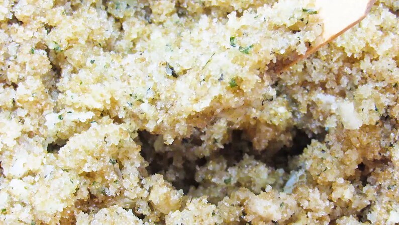 Close-up view of peppermint and coconut cane sugar scrub in a bowl with a wooden spatula, highlighting its grainy texture and details of green mint and coconut shavings.