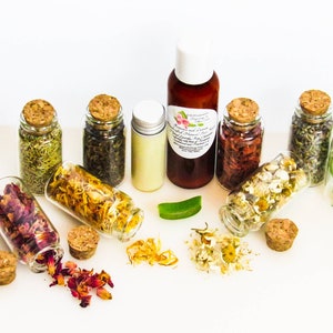 An all-natural facial cleanser in an amber bottle surrounded by eight small corked glass bottles containing sprinkles of Calendula, Rose, Lavender, Chamomile, Rosemary, Aloe Vera, Sandalwood and Patchouli ingredients and sprinkles of the same.