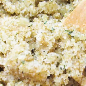 Close-up view of peppermint and coconut cane sugar scrub in a bowl with a wooden spatula, highlighting its grainy texture and details of green mint and coconut shavings.