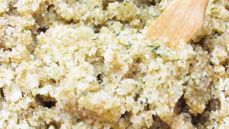Close-up view of peppermint and coconut cane sugar scrub in a bowl with a wooden spatula, highlighting its grainy texture and details of green mint and coconut shavings.