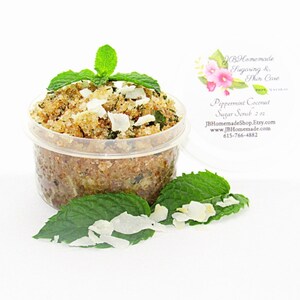A 2 oz tub of cooling peppermint and coconut cane sugar scrub offers a refreshing and hydrating experience for your skin. The sugar scrub is centered, near bright green sprigs of peppermint and coconut flakes are scattered throughout the arrangement.