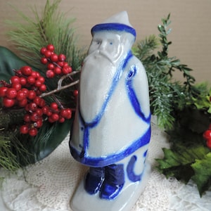 May include: A ceramic figurine of a bearded figure wearing a pointed hat, a long coat, and boots. The piece features a light gray glazed finish with vibrant cobalt blue painted accents along the edges of the clothing, hat, and footwear.