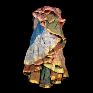 Könnte beinhalten: Ein mehrlagiger Rock aus verschiedenen Stoffbahnen mit Mustern in Blau-, Grün-, Rosa- und Brauntönen. Jede Stufe weist komplexe Designs auf und ist an den gerüschten Kanten mit einer metallisch goldfarbenen Borte versehen.