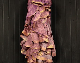 May include: A long, flowing skirt with multiple layers of ruffles. The skirt is made of a purple and gold fabric with a floral pattern. The skirt is gathered at the waist and falls to the floor.