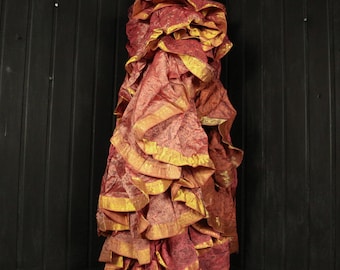 May include: A ruffled, floor-length dress in shades of red and gold. The dress features multiple layers of fabric with gold trim along the edges. The fabric has a textured appearance, and the dress is displayed on a black mannequin against a dark background.