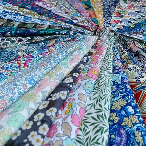 May include: A collection of various fabric swatches, arranged in a circular pattern. The fabrics display a range of floral and botanical patterns in a variety of colors, including blue, pink, green, and white. The fabrics are likely cotton or linen.