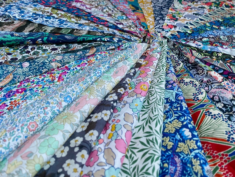 May include: A collection of various fabric swatches, arranged in a circular pattern. The fabrics display a range of floral and botanical patterns in a variety of colors, including blue, pink, green, and white. The fabrics are likely cotton or linen.