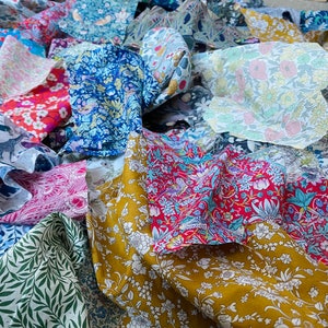 May include: A collection of colorful floral patterned fabrics in various shades of blue, red, yellow, and green. The fabrics are arranged in a pile, showcasing a variety of designs, including botanical and animal prints. The textiles appear to be cotton or a similar lightweight material.