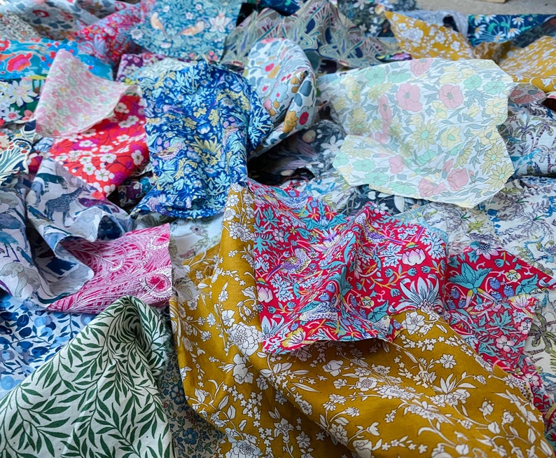 May include: A collection of colorful floral patterned fabrics in various shades of blue, red, yellow, and green. The fabrics are arranged in a pile, showcasing a variety of designs, including botanical and animal prints. The textiles appear to be cotton or a similar lightweight material.