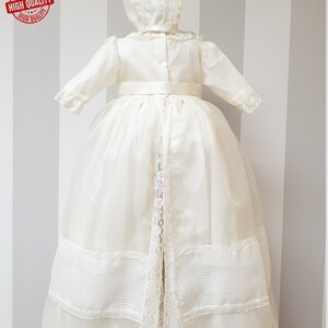 Peut inclure: Une robe de bapt&ecirc;me blanche avec une bordure en dentelle et une ceinture en satin. La robe est assortie &agrave; un bonnet avec une bordure en dentelle.