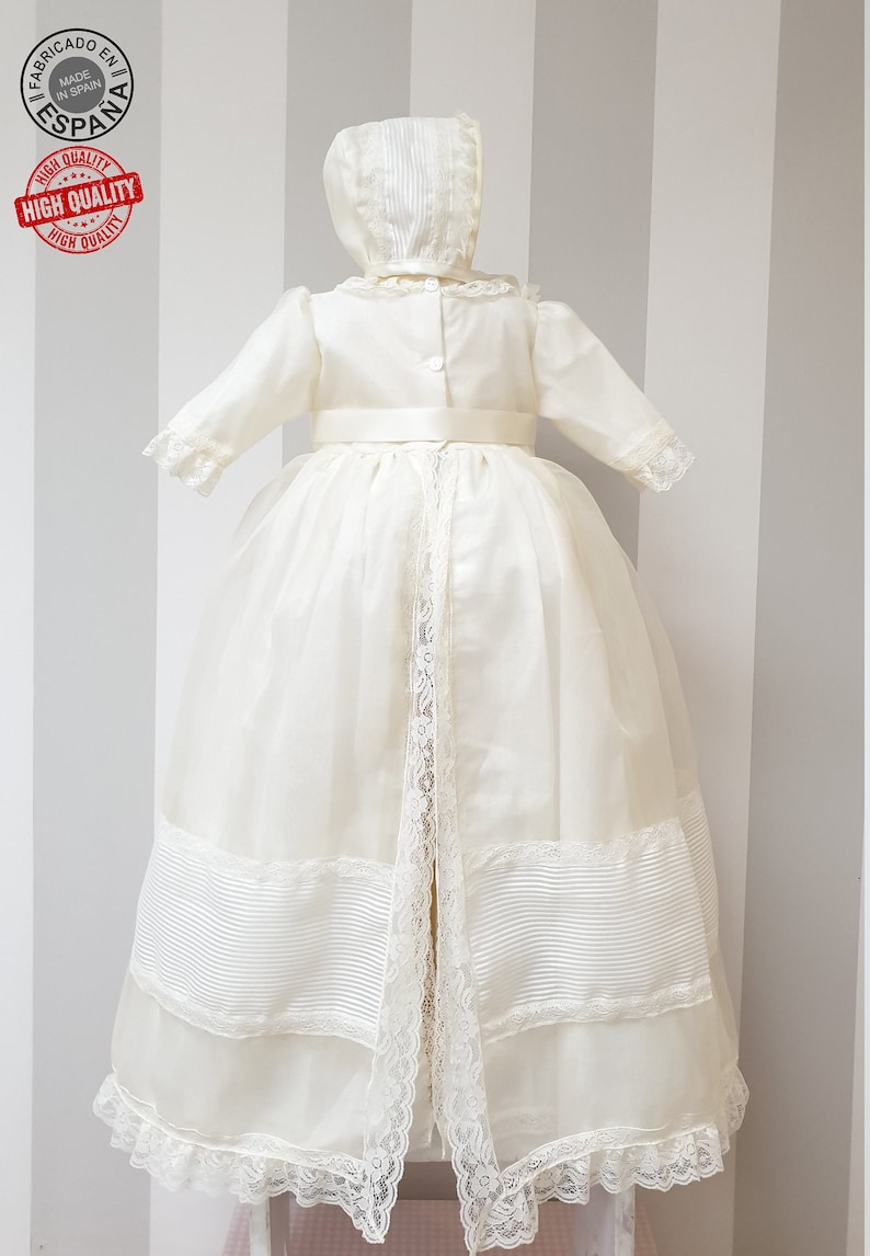 Peut inclure: Une robe de bapt&ecirc;me blanche avec une bordure en dentelle et une ceinture en satin. La robe est assortie &agrave; un bonnet avec une bordure en dentelle.