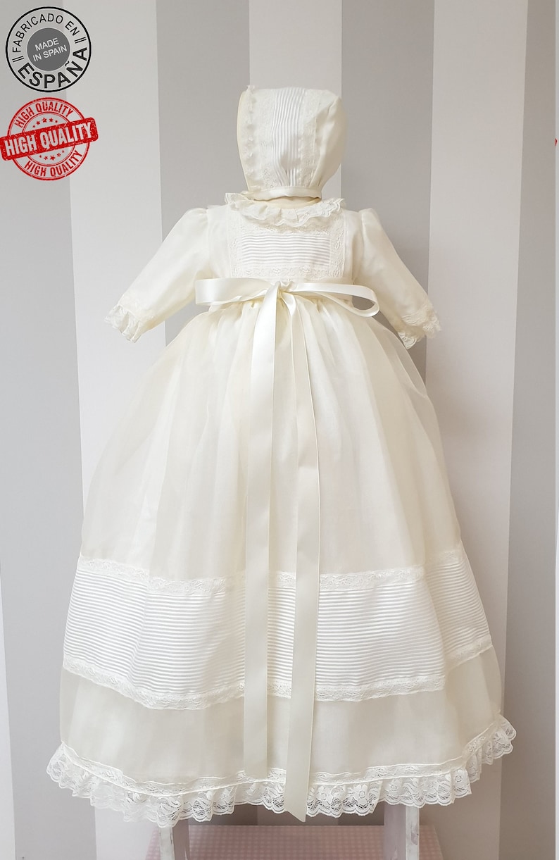 Peut inclure: Une robe de bapt&ecirc;me blanche avec une bordure en dentelle et un ruban de satin. La robe est assortie &agrave; un bonnet avec une bordure en dentelle.