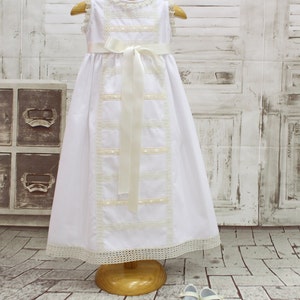 White Baptism dress, white Christening gown in white pique with ivory laces. Sleeveless. Cotton laces in ivory With satin bow waist.