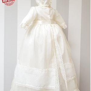 Peut inclure: Une robe de bapt&ecirc;me blanche avec une bordure en dentelle et une ceinture en satin. La robe est assortie &agrave; un bonnet.
