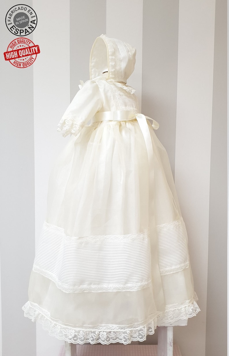 Peut inclure: Une robe de bapt&ecirc;me blanche avec une bordure en dentelle et une ceinture en satin. La robe est assortie &agrave; un bonnet avec une bordure en dentelle.