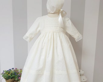 Elfenbeinfarbenes Taufkleid aus Plumeti-Baumwolle. Mit passendem Hut. Lange Ärmel. Elfenbeinfarbener Spitzenbesatz. Taufkleid im spanischen Stil. Haube.