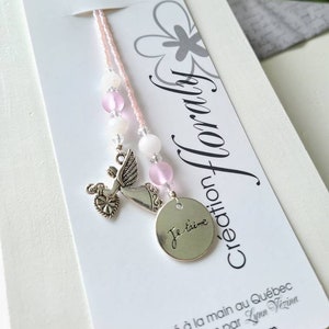 Peut inclure: Marque-page rose en perles avec un charm en argent représentant une colombe tenant un cœur et un pendentif rond avec l'inscription "Je t'aime". Le marque-page est fixé à une carte blanche avec des motifs floraux.