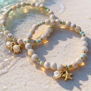 May include: Two beaded bracelets featuring white marbled beads, small light blue accent beads, and gold-toned spacers. One bracelet includes a gold-toned sea turtle charm and a white pearl, while the other features a gold-toned starfish and a white pearl.