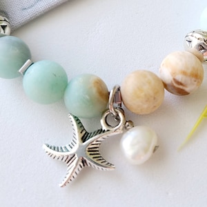 May include: A bracelet with light blue and brown beads, a silver starfish charm, and a white pearl charm.