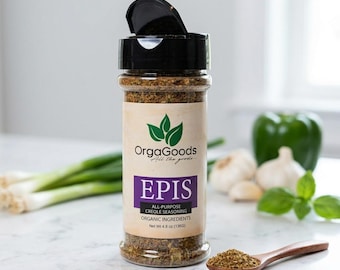 May include: A clear spice jar with a black lid, labeled "EPIS" and "All-Purpose Creole Seasoning." The label also reads "OrgaGoods" and "Organic Ingredients." A wooden spoon holds a small pile of the seasoning. Green onions, garlic, and a green pepper are in the background.