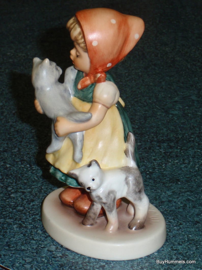 Puede incluir: Una figurita de una ni&ntilde;a con un vestido de lunares rojos y blancos que sostiene dos gatitos. La ni&ntilde;a lleva un vestido de lunares rojos y blancos y un sombrero de lunares rojos y blancos. Los gatitos son grises y blancos.