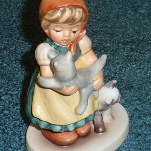 Puede incluir: Una figurita de porcelana de una ni&ntilde;a con un vestido rojo y verde que sostiene dos gatitos. La ni&ntilde;a tiene el pelo rubio y lleva una capucha roja. Los gatitos son grises y blancos.