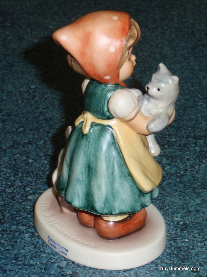 Puede incluir: Una figurita de una ni&ntilde;a con un vestido rojo con lunares blancos y un gorro rojo que sostiene un gatito gris. La figurita est&aacute; sobre una base blanca con las palabras "Katzenmama Tender Love" escritas en ella.