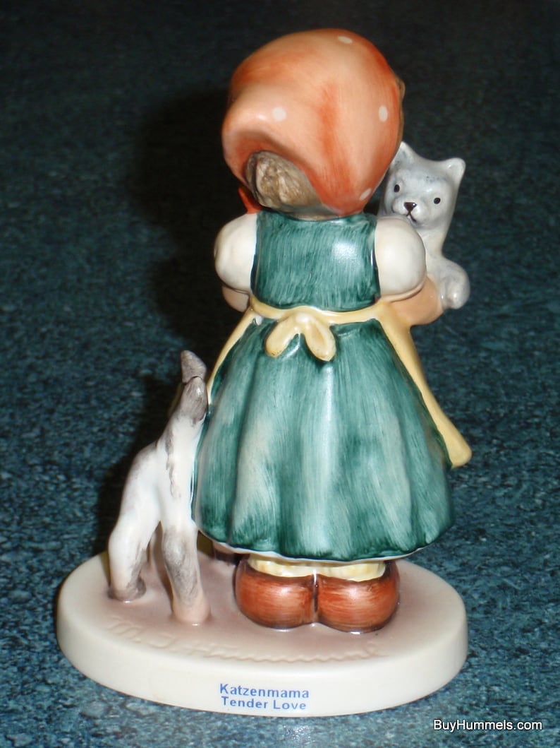 Puede incluir: Una figurita de una ni&ntilde;a con un vestido rojo con lunares blancos y un sombrero rojo que sostiene dos gatitos. La figurita est&aacute; sobre una base blanca con las palabras "Katzenmama Tender Love" escritas en ella.