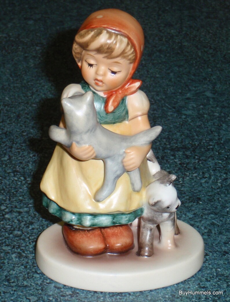 Puede incluir: Una figurita de porcelana de una ni&ntilde;a con un vestido rojo y blanco que sostiene un gato gris y un perro marr&oacute;n y blanco. La ni&ntilde;a lleva una diadema roja y blanca y un lazo rojo.