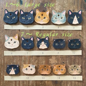 May include: A collection of fifteen cat-shaped leather tags arranged in three rows, labelled 1 through 15. The top row, labelled 1-6 Large size, features five cat faces. The middle row, labelled 7- Regular size, shows five more. The bottom row shows five.