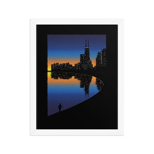 May include: A framed art print featuring a stylized Chicago skyline silhouette at dusk with a gradient orange and blue sky. The city lights reflect on the water below, while a small dark figure of a person runs along the curved shoreline.