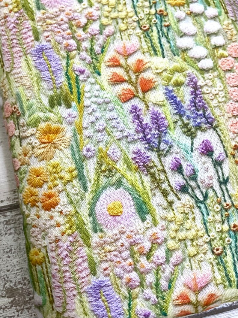 Puede incluir: Un primer plano de una tela blanca con flores bordadas en tonos de rosa, morado, amarillo y verde. Las flores est&aacute;n dispuestas en un patr&oacute;n aleatorio y crean un dise&ntilde;o hermoso y delicado.