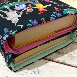 May include: Two book covers with a dark background featuring a colorful illustration of characters from The Wizard of Oz. The covers are decorated with floral patterns and have pink and light blue linings.