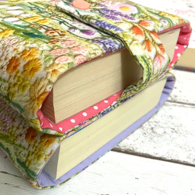Puede incluir: Un libro con una cubierta de tela con estampado floral. La cubierta tiene un bot&oacute;n rosa y una correa. El libro est&aacute; apilado encima de otro libro con una cubierta de tela de lunares rosa y blanco.