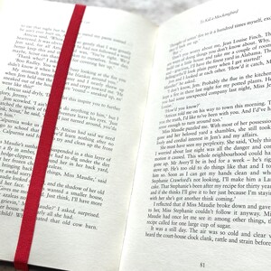 May include: Open book with a red bookmark. The book is open to page 81 and the text reads "How'd you know?"  "Atticus told me on his way to town this morning. Tell you the truth, I'd like to've been with you. And I'd've had enough to turn around too."