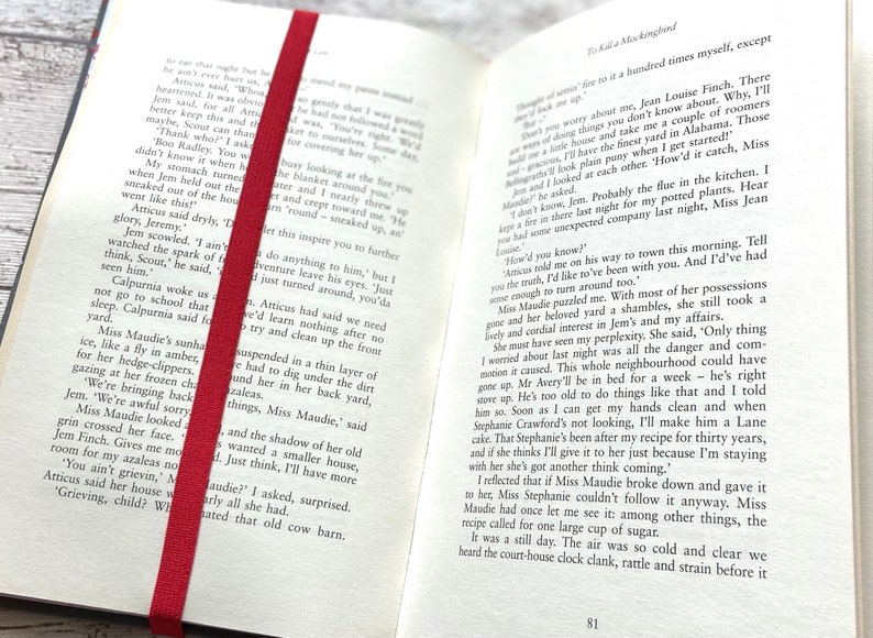 May include: Open book with a red bookmark. The book is open to page 81 and the text reads "How'd you know?"  "Atticus told me on his way to town this morning. Tell you the truth, I'd like to've been with you. And I'd've had enough to turn around too."