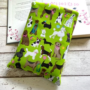 Può includere: Una custodia per libri verde lime con un motivo ripetuto di varie razze di cani, tra cui barboncini e bassotti. I cani sono adornati con accessori come bandane e cappelli da festa, e sono intervallati da palline colorate. La custodia è progettata per proteggere i libri.