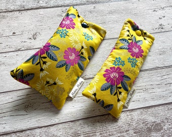 May include: Two yellow fabric pouches with floral patterns. The pouches feature a design of pink, blue, and white flowers with silver accents. Each pouch has a button closure and a small tag that reads "Melvis Makes".