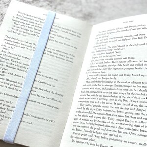 May include: Open book with a light blue bookmark. The book is open to a page with text about a play. The text includes the names Penelope Gunnerslake and Charlie Wetherall.
