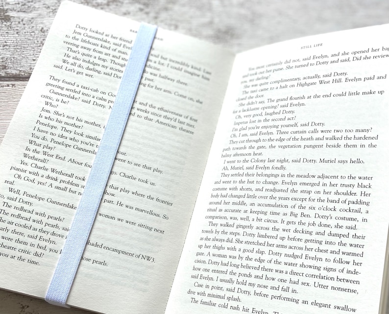 May include: Open book with a light blue bookmark. The book is open to a page with text about a play. The text includes the names Penelope Gunnerslake and Charlie Wetherall.