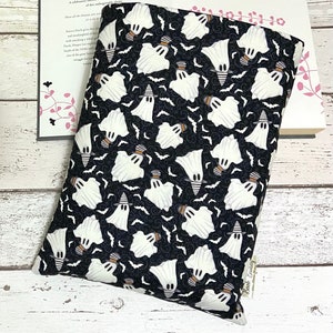 Puede incluir: Cubierta de libro negra con un patrón de fantasmas blancos. Los fantasmas llevan sombreros de bruja y vuelan sobre un fondo negro con murciélagos y remolinos. La cubierta del libro tiene una pequeña etiqueta blanca con el texto "Book Buddy" en ella.