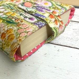 Puede incluir: Una cubierta de libro con un patr&oacute;n floral en tonos de verde, amarillo, rosa y morado. La cubierta tiene un bot&oacute;n rosa y un forro de lunares rosa y blanco.