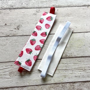 May include: Two fabric book markers, one with a white background and red strawberries, the other plain white with a white elastic band.