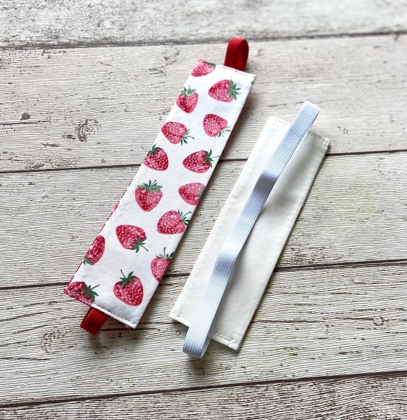 May include: Two fabric book markers, one with a white background and red strawberries, the other plain white with a white elastic band.