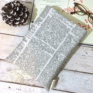 May include: A white book cover with a black and white newspaper print design. The cover has a small brown tag with the text "Book Binding" on it.