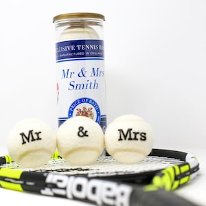 May include: Three white tennis balls with black lettering, reading "Mr", "&", and "Mrs" are on a black and yellow tennis racket. A glass jar with a gold lid contains more tennis balls and reads "Mr & Mrs Smith".