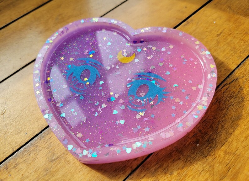 May include: A heart-shaped resin tray with a glittery purple and pink gradient. The tray features two blue eyes with eyelashes and a crescent moon.