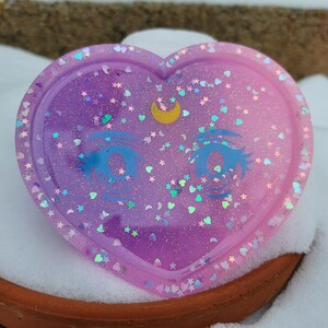 May include: A heart-shaped resin tray with a gradient of pink and purple glitter. The tray features a crescent moon and a pair of anime eyes.